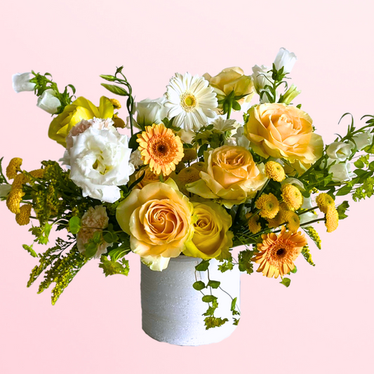 This is a lush arrangement featuring a mix of yellow, gold, and cream premium blooms and accent flowers with fresh garden greens elegantly designed in a ceramic vase.
