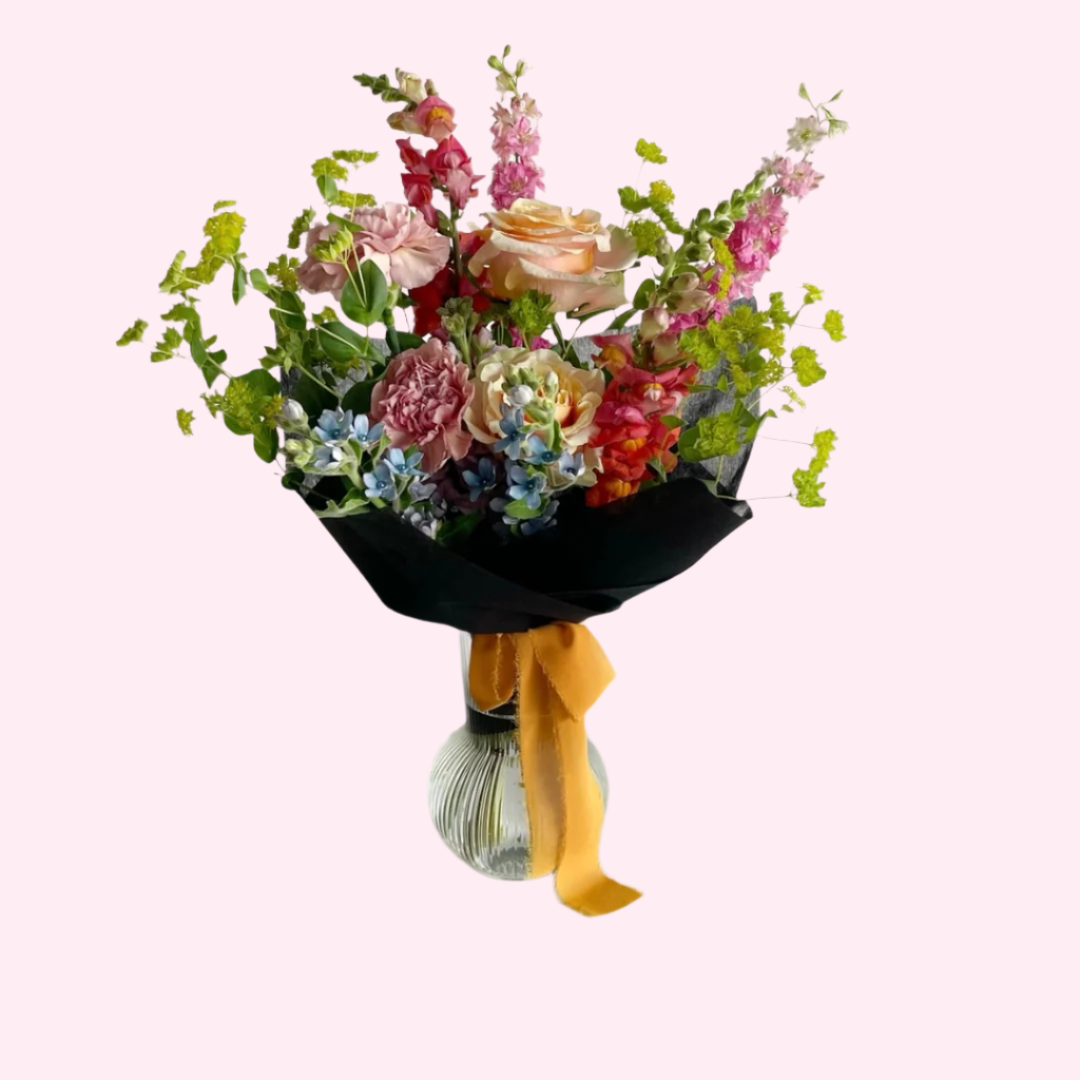 A mix of colorful and in season blooms and greenery wrapped in black paper and tied with a bow.