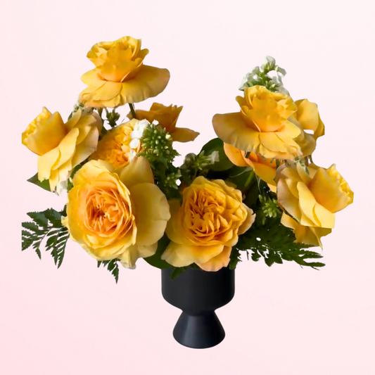 A Dozen premium roses designed in an artful shape mixed with foliage and placed in a modern black ceramic vessel.
