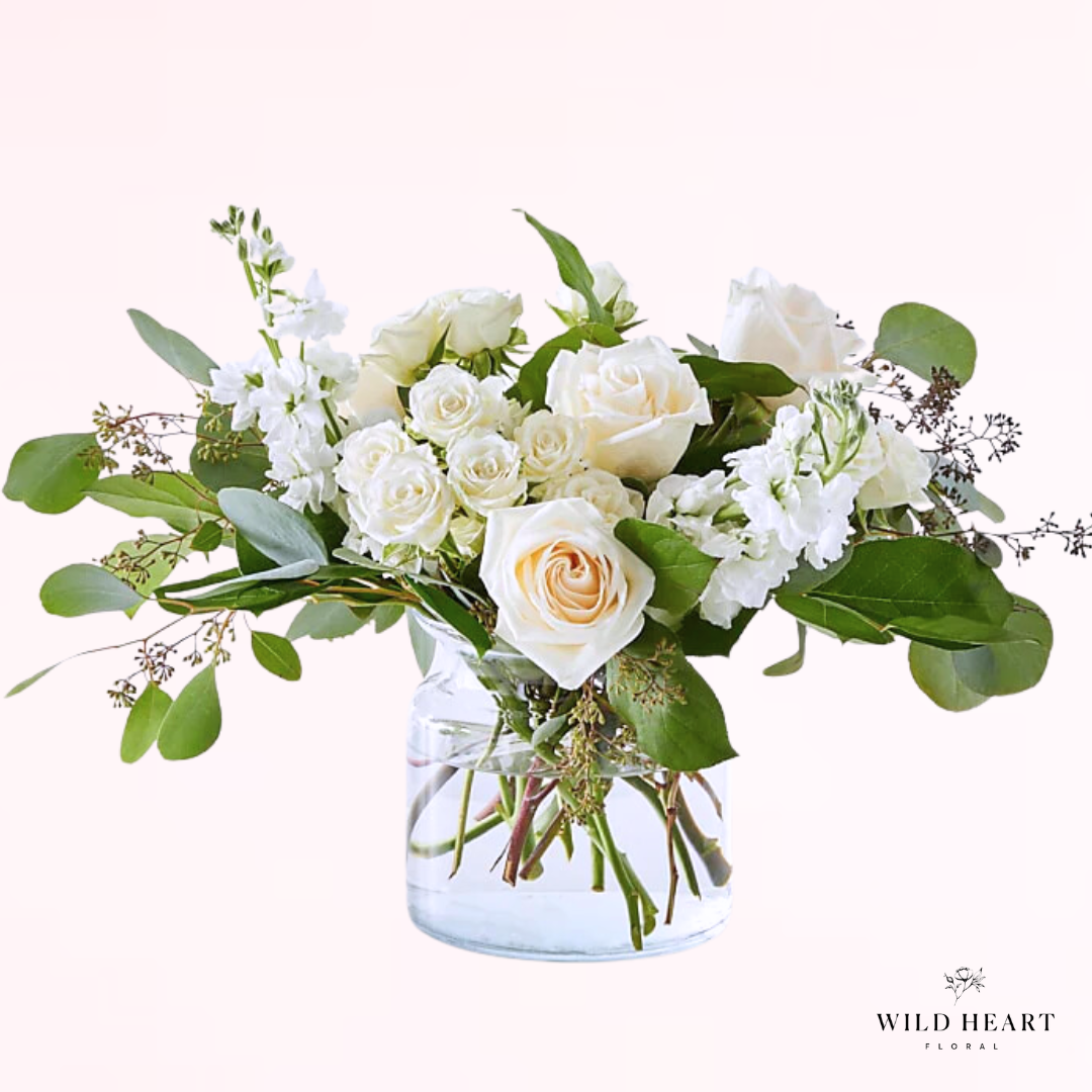A classic garden style sympathy arrangement with mix of white spray roses, white premium roses, white stock, and mix of elegant foliage's complete with a classic glass cylinder vase.