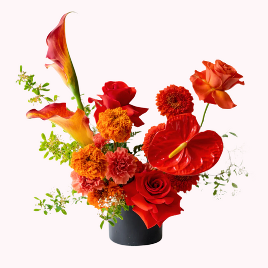 A fiery mix of premium assorted flowers with foliage and designed in an elegant and modern shape complete with a black ceramic vase